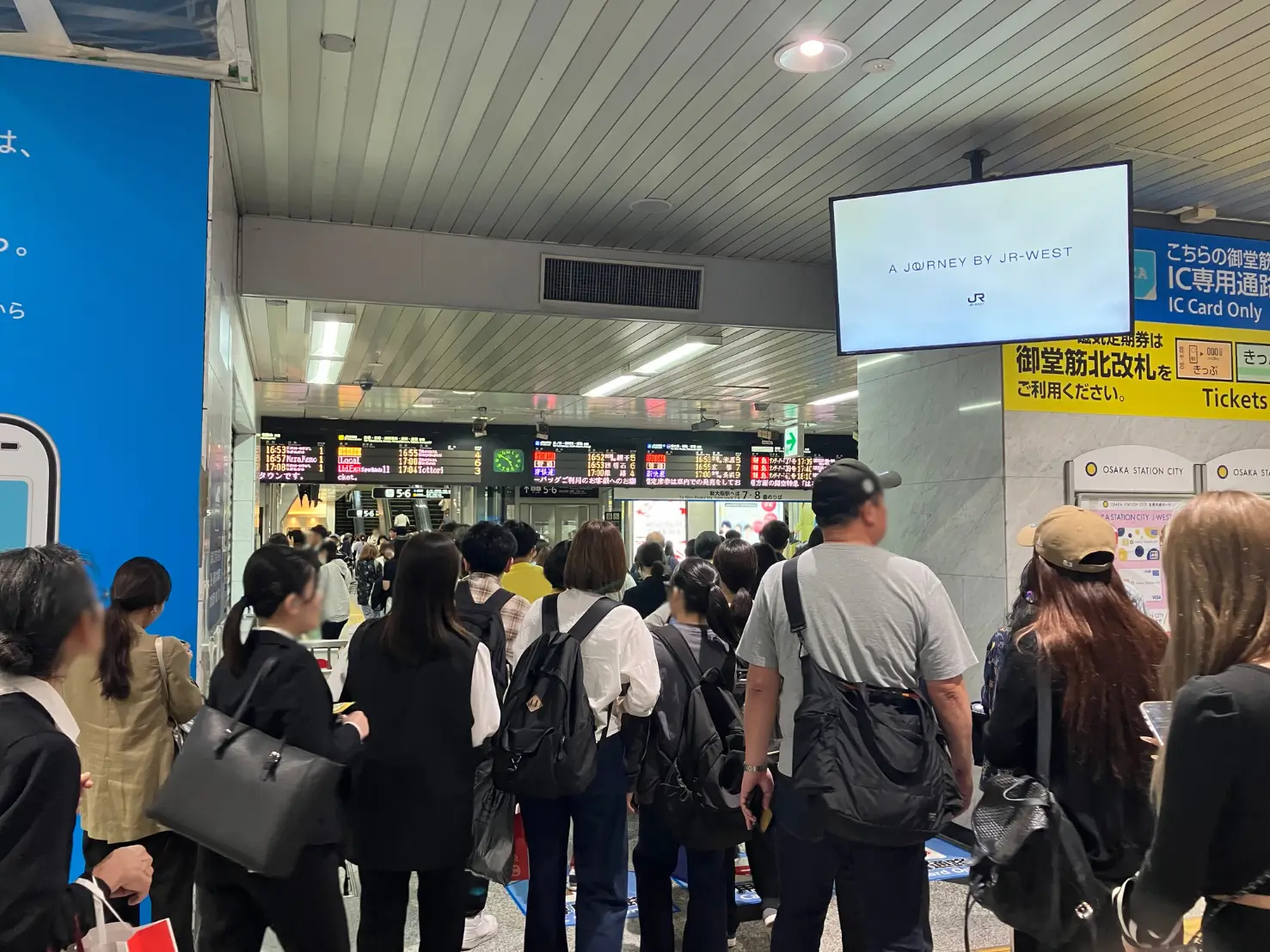 JR大阪駅の御堂筋口改札を行き交う多くのビジネスパーソンと駅のデジタルサイネージ広告