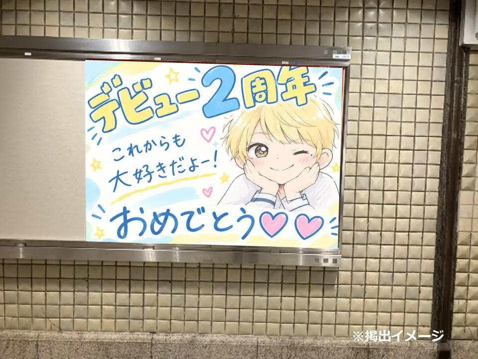 駅構内のポスターフレームに掲出された「デビュー2周年おめでとう」のイラスト入り応援広告ポスター（近景）